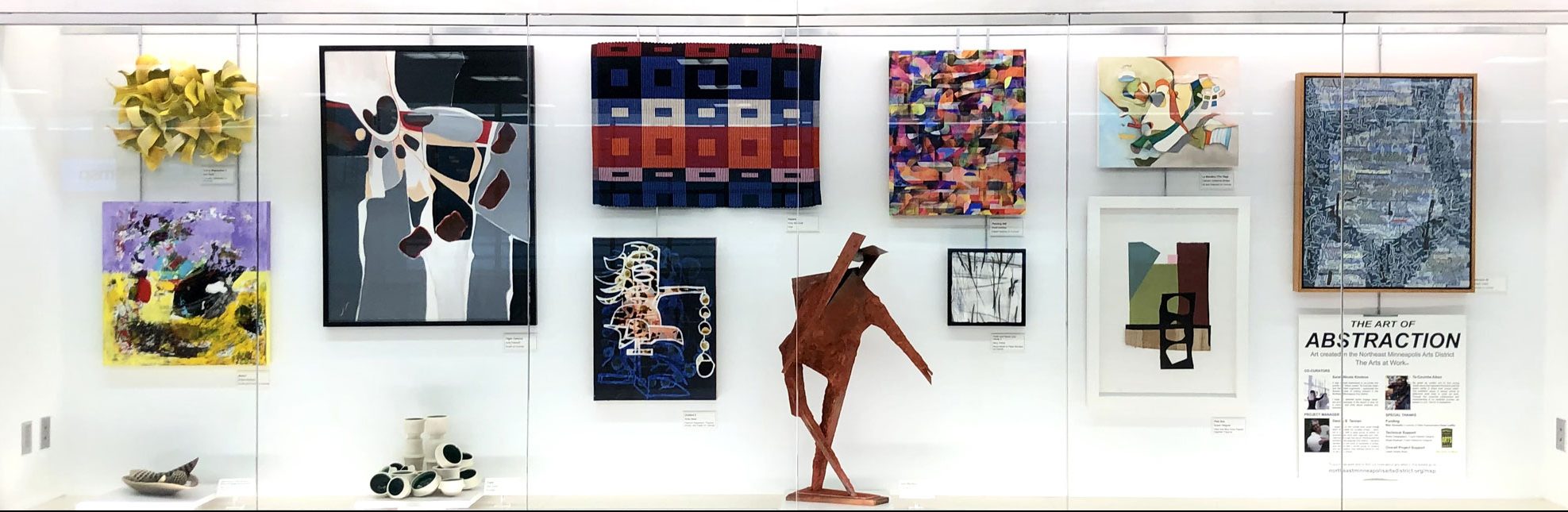 An installation image from a previous exhibition at the airport, showing a number of visual works hung from the wall and standing as sculptures within a large glass display case.