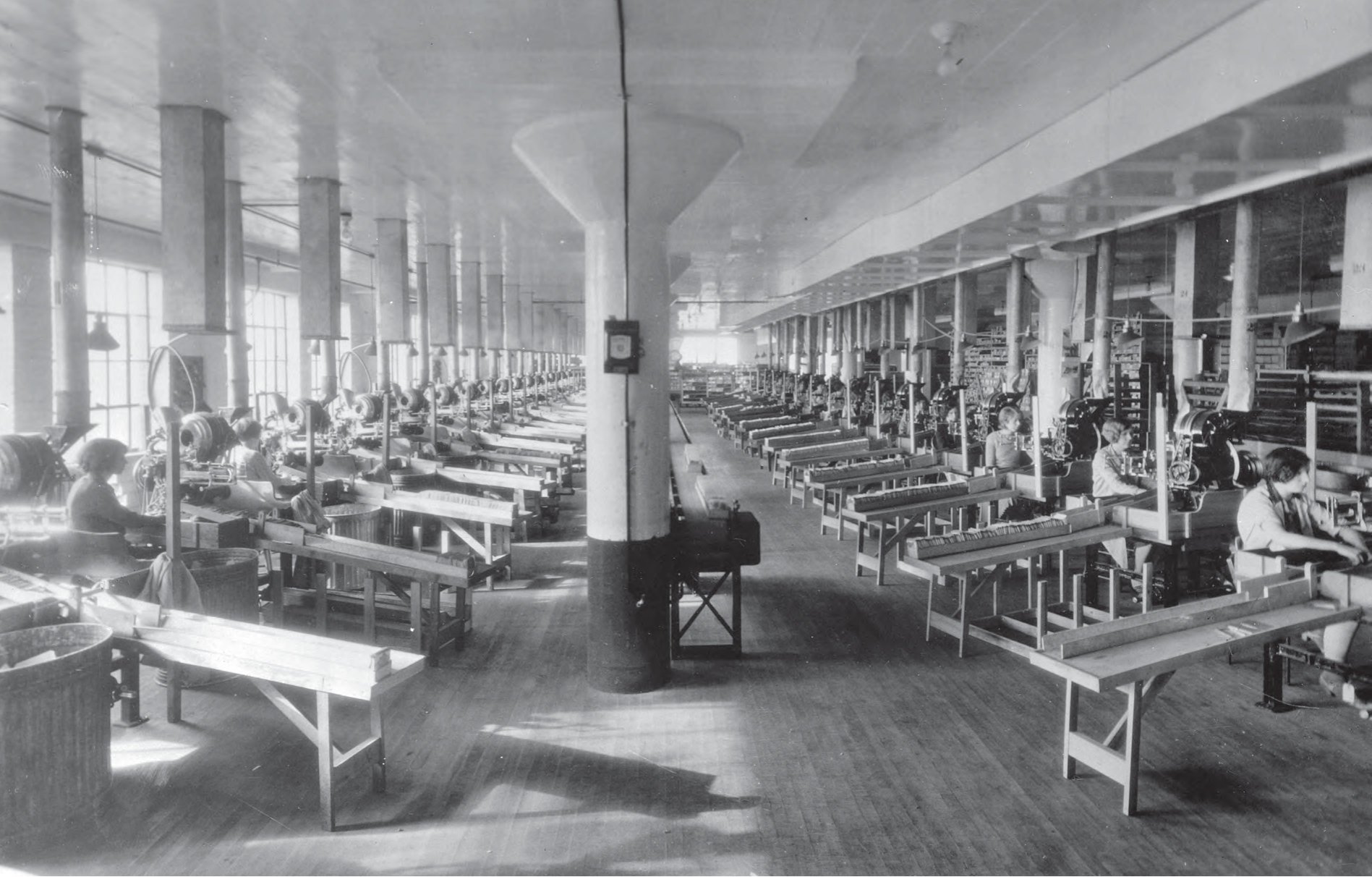 Historic photo of rows of workers at long tables inside the Northrup King Company factory