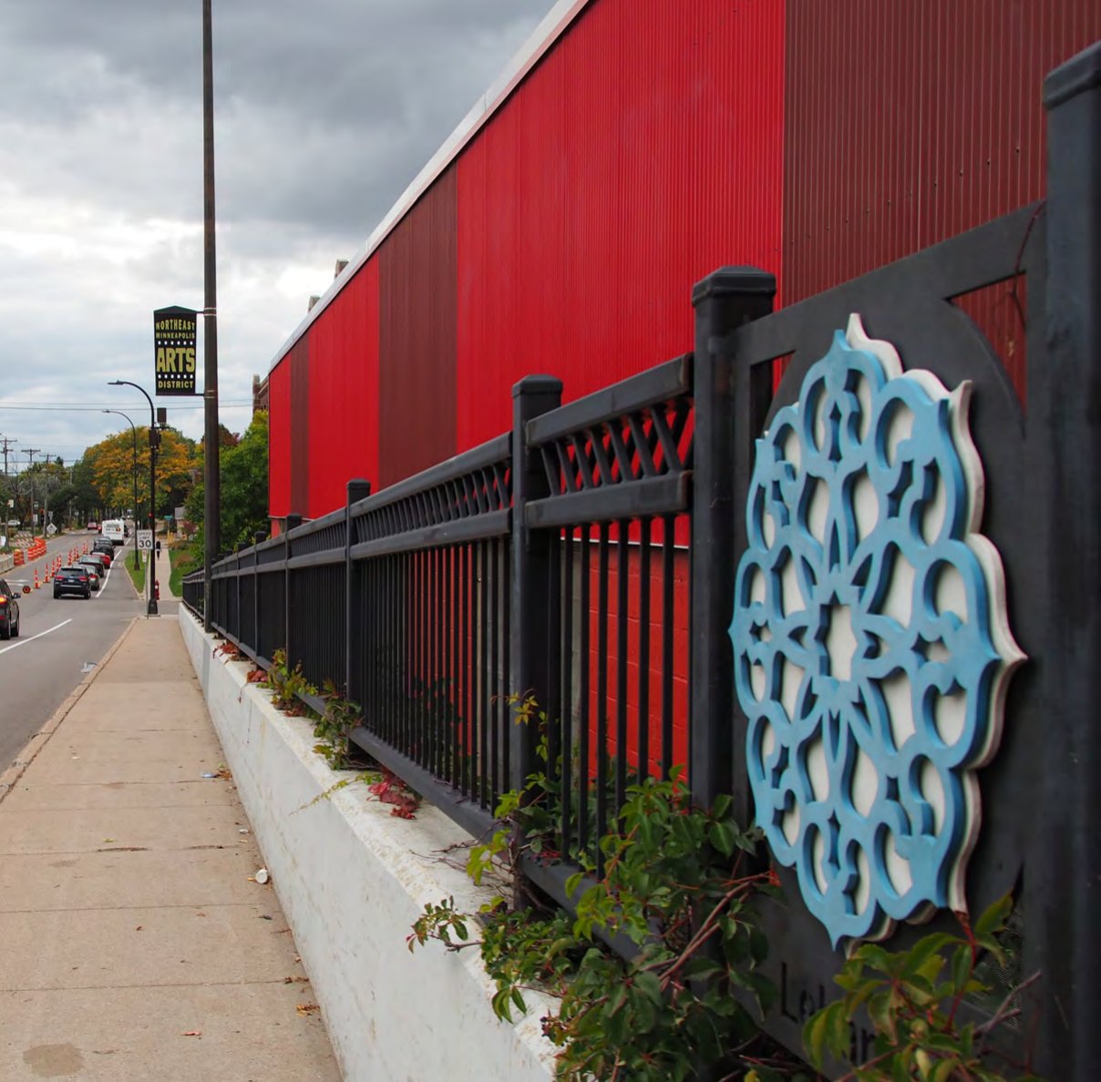 Blue ethnic motif set into a black wrought iron fence along a sidewalk