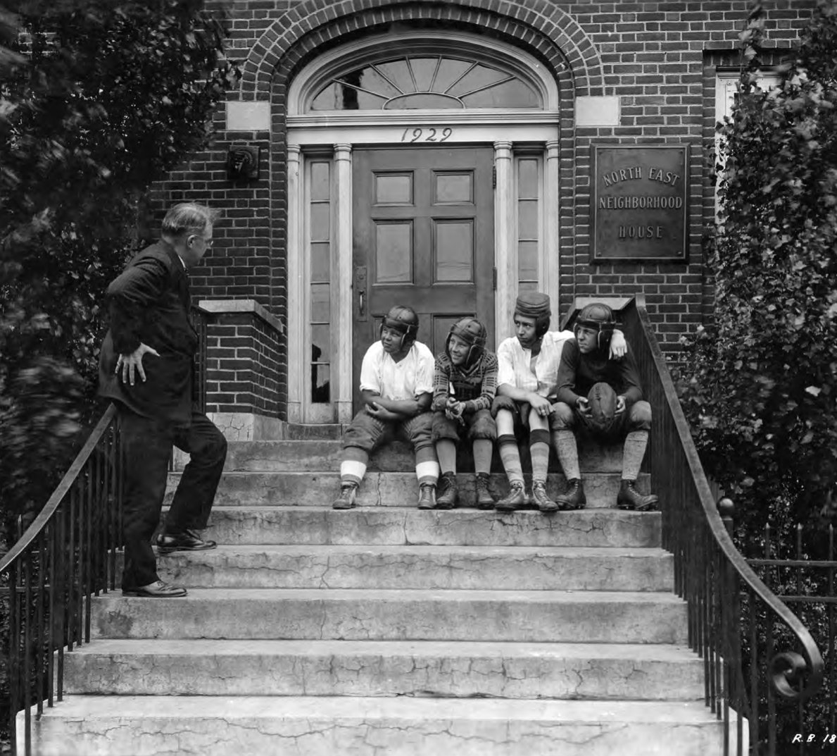 Historic photo of boys in football helmets sitting on the front steps of the Northeast Neighborhood House