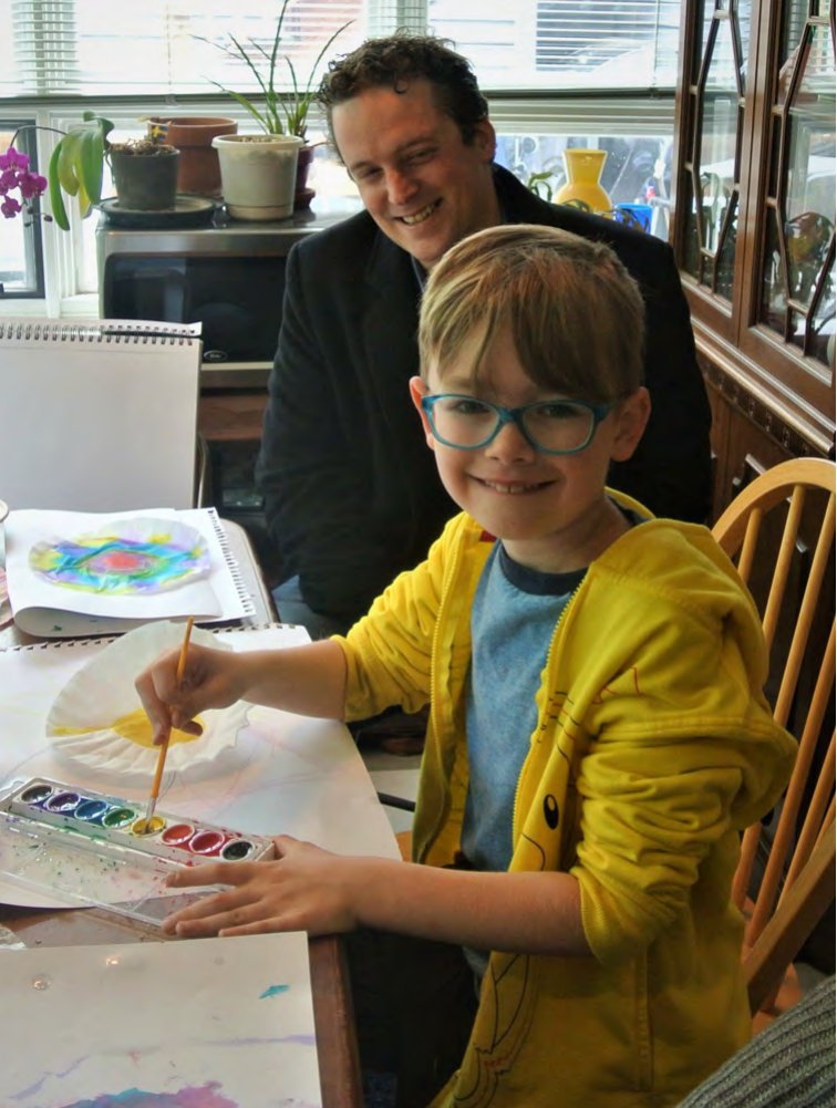 A child painting with watercolors while an adult watches