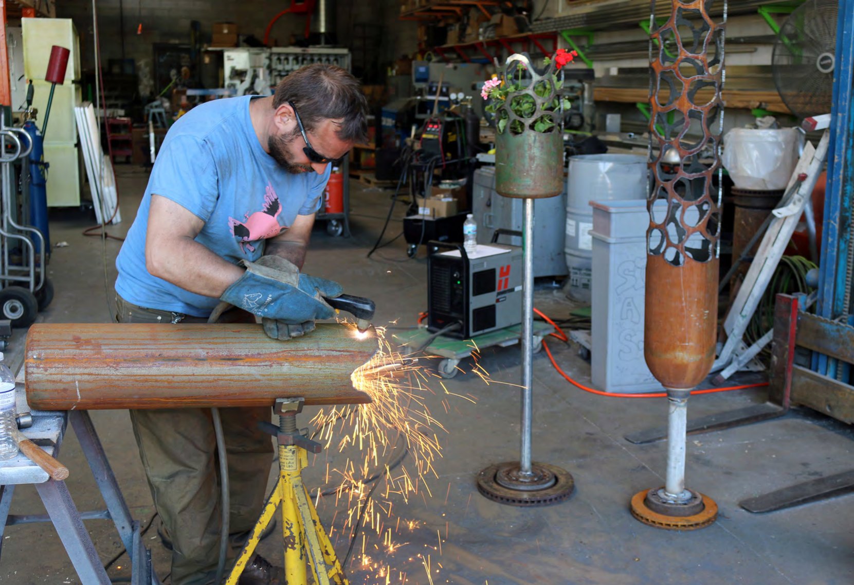 Ben Janssens cutting metal with sparks flying, finished planters behind him