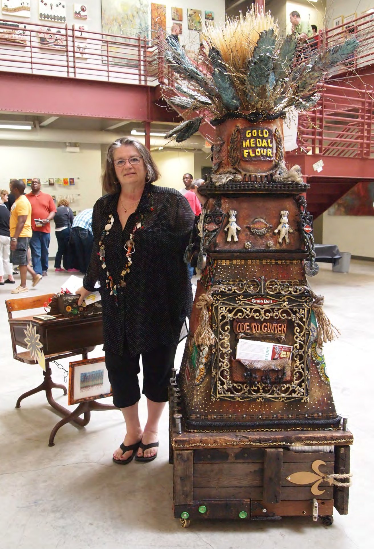 Barbara Bridges standing beside her tall assemblage sculpture Ode to Gluten