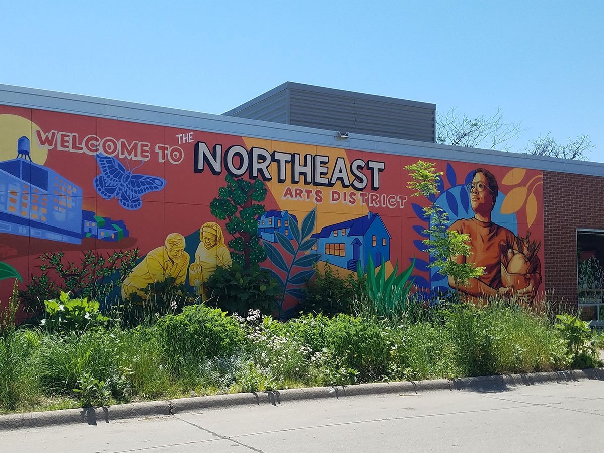 Eastside food co-op mural with a butterly, people, and brick buildings.