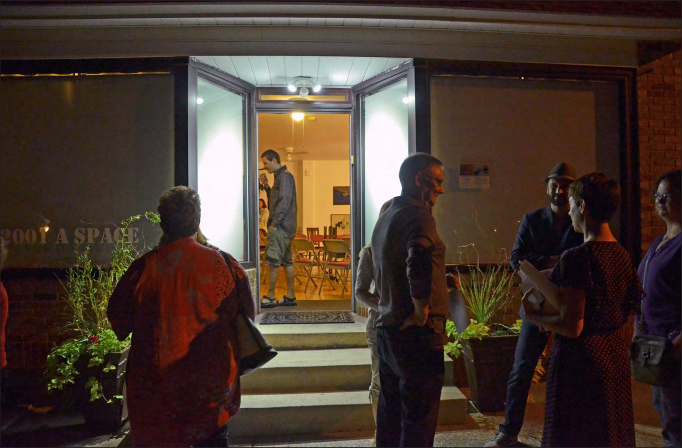 Visitors gathered outside the lit doorway of 2001 A SPACE gallery at night