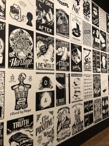 A wall covered in a grid of black-and-white graphic posters featuring protest art, illustrations, and text about social issues.