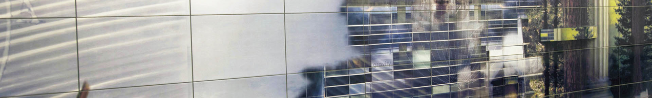 A modern building facade featuring a grid of glass windows reflecting clouds and trees.