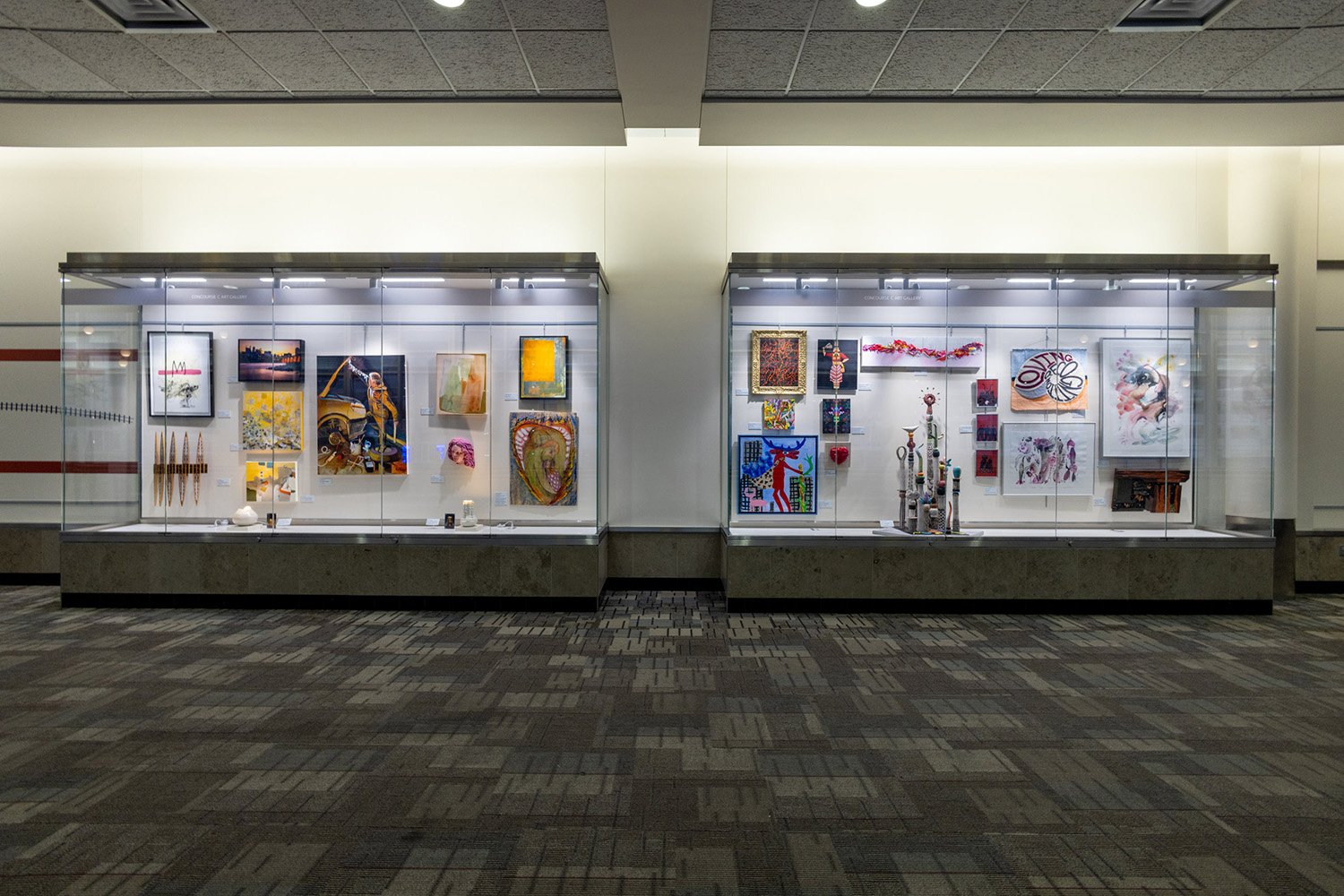 Two large glass display cases housing various framed artworks and sculptures in a hallway.