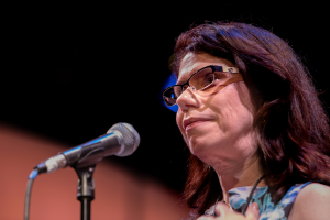 A woman wearing glasses speaks into a microphone.