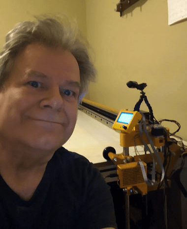 A man taking a selfie next to a yellow quilting machine.
