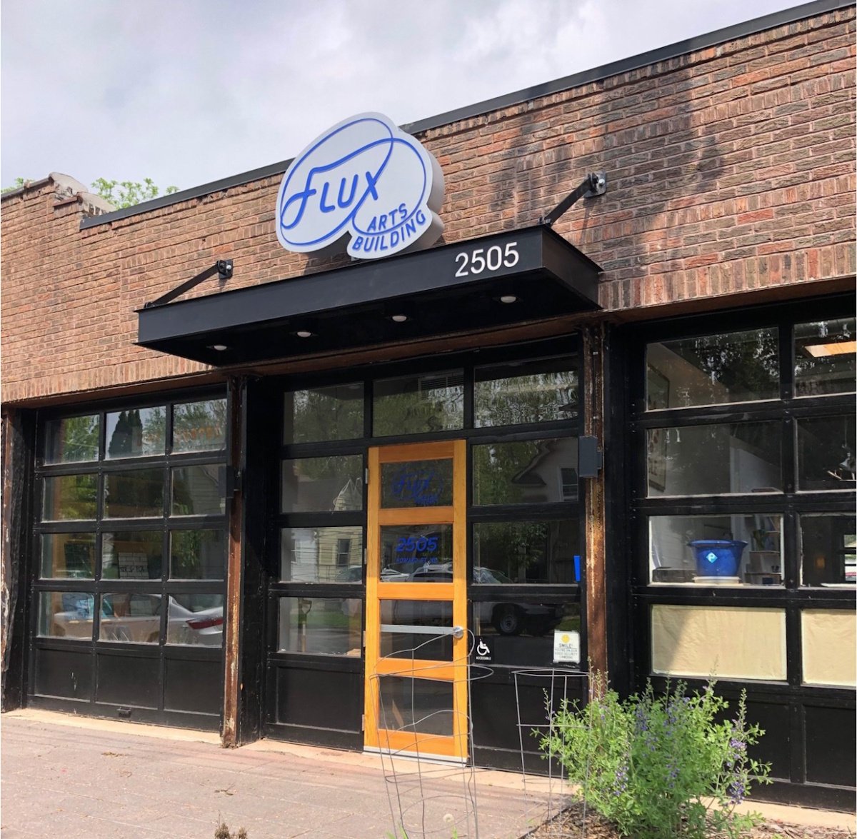 The brick facade of the Flux Arts Building at 2505 with a black awning and a wooden front door.