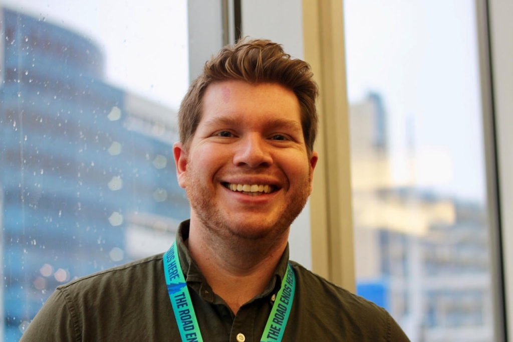 A smiling man wearing a lanyard that reads The Road Ends Here.