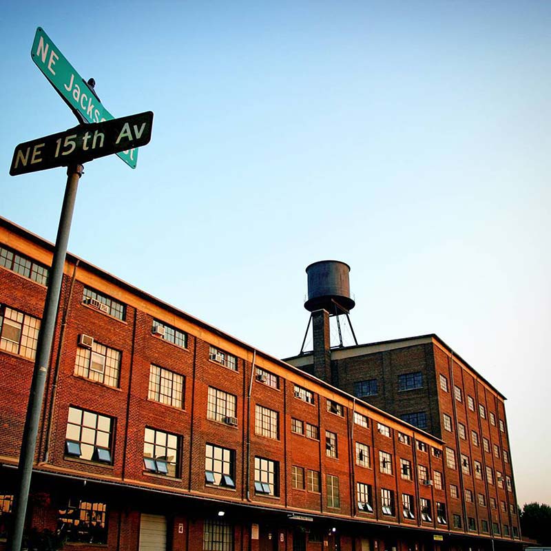 A multi-story brick factory building with a water tower on the roof, next to a street sign for NE 15th Ave and NE Jackson St.