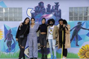Five people pose for a photo in front of a colorful wall mural.