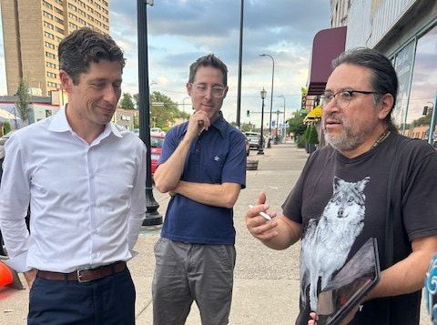 Three men having a conversation on a city sidewalk.