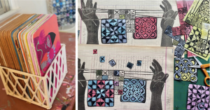 A white plastic crate holding a stack of colorful illustrated cards sits next to an art project featuring prints of hands holding strings with hanging geometric pattern squares.